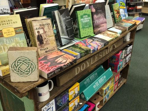 A wooden display table filled with various books, including titles about Ireland and notable authors, in a cozy bookstore.