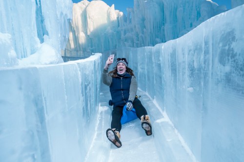 A person joyfully sledding down an icy slide, surrounded by towering ice formations.
