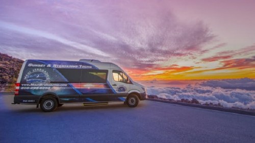 A tour van parked on a scenic overlook with a colorful sunset and clouds in the background.