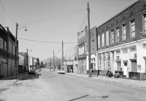 Black and white photo of a deserted street with old buildings, parked cars, and a movie theater marquee in the distance.