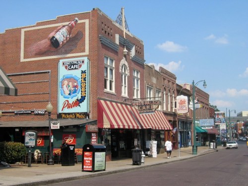 A vibrant street scene featuring historic buildings, cafes, and colorful signage under a clear blue sky.