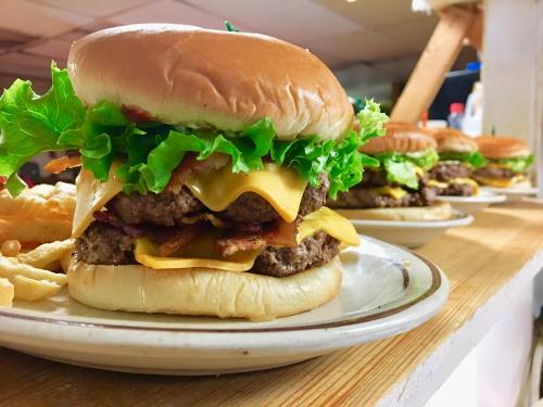 A close-up of a stacked cheeseburger with lettuce, bacon, and melted cheese on a bun, served on a plate.