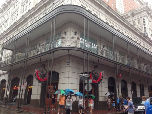 Historic building with a balcony, people walking with umbrellas, and a restaurant entrance on a rainy day.