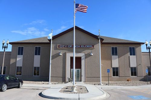 City of Box Elder building with an American flag in front, clear blue sky, and accessible parking.