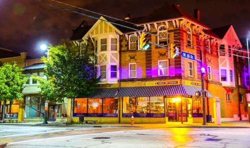 A brightly lit street corner at night featuring a historic building with shops and trees, illuminated by streetlights.
