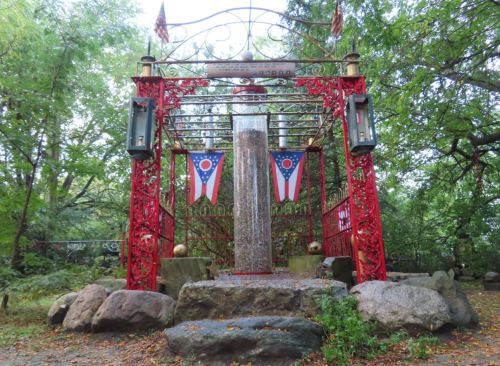 A decorative red structure with Ohio flags, surrounded by rocks and trees in a serene outdoor setting.