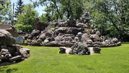 A rocky landscape with large boulders and sculptures, surrounded by green grass and trees under a clear blue sky.