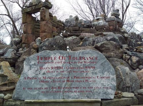 Stone monument with engraved text about the "Temple of Tolerance," surrounded by a rocky structure and trees.
