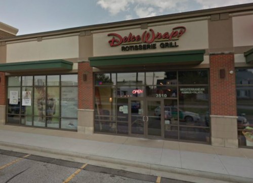 Exterior of Dolce Wraps Rotisserie Grill, featuring large windows and an "OPEN" sign, located in a shopping plaza.