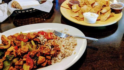 A plate of chicken stir-fry with rice and a side of tortilla chips with dips on a table.