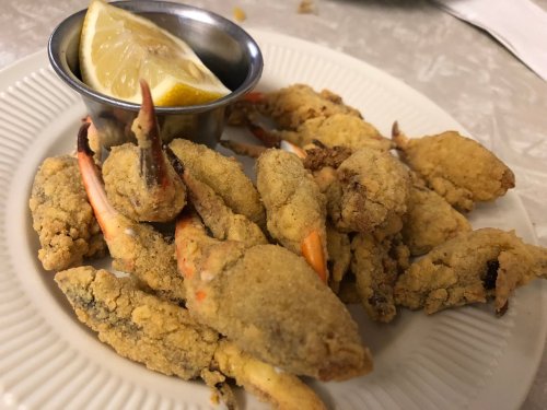 A plate of fried crab claws served with a lemon wedge and a small cup of dipping sauce.