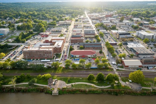 Aerial view of a small town with buildings, trees, and a river, bathed in warm sunlight.