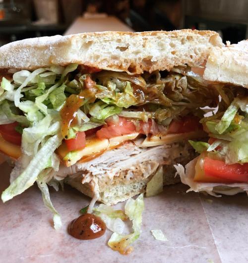 Close-up of a sandwich filled with turkey, lettuce, tomatoes, and sauce, served on thick bread.