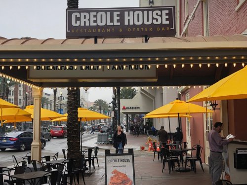 Exterior of Creole House restaurant with yellow umbrellas, palm trees, and a street view in a rainy setting.