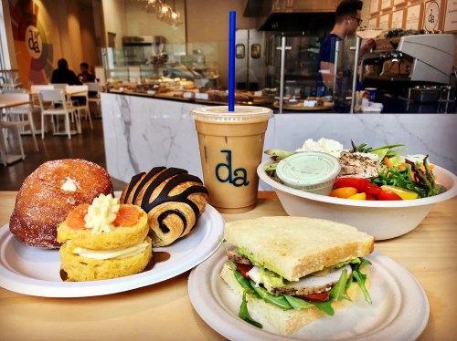 A table with a variety of food: pastries, a sandwich, a salad, and an iced drink in a café setting.