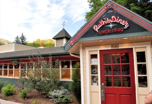Exterior of Rusty's Diner, featuring a red door and sign, surrounded by greenery and trees. Established in 1939.