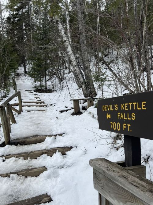 A snowy trail leads to Devil's Kettle Falls, marked by a wooden sign indicating the distance of 700 feet.