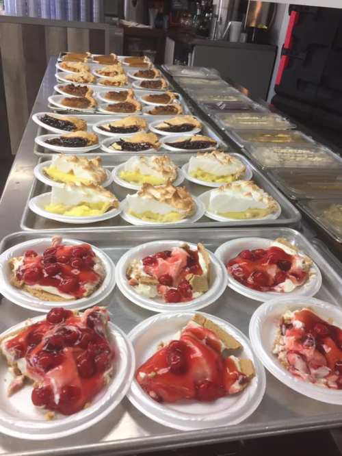 A display of various desserts on plates, including cherry pie and lemon meringue, arranged on a counter.