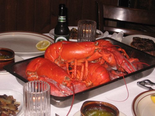 A platter of cooked lobsters on a dining table, accompanied by drinks and side dishes.