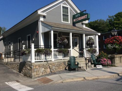 A charming restaurant with a gray exterior, flower baskets, and a welcoming porch, set in a sunny outdoor environment.