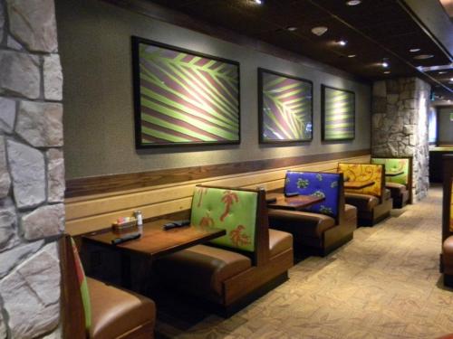 Colorful booths with tropical designs line a restaurant wall, featuring framed artwork above and a stone accent.