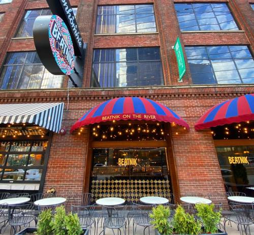 Exterior of Beatnik on the River, featuring a red and blue awning, outdoor seating, and large windows.
