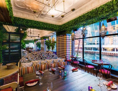A vibrant restaurant interior with greenery, colorful decor, and a large window overlooking a river.