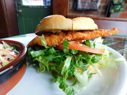 A close-up of a crispy chicken sandwich with lettuce and tomato, served with a side of coleslaw.