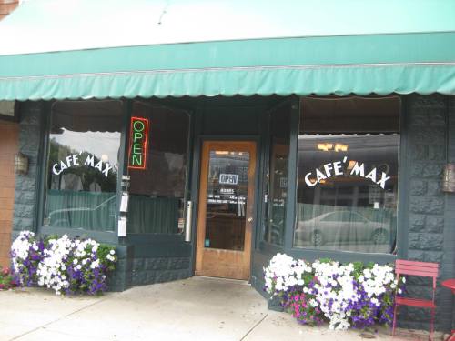 Exterior of Cafe Max with a green awning, open sign, and flower beds in front.