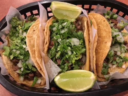 A black basket filled with three tacos topped with cilantro, onions, and lime wedges.