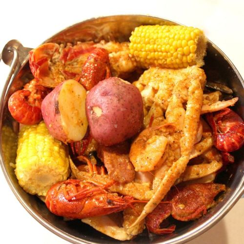 A bowl filled with a variety of seafood, including crab, crawfish, corn, and potatoes, seasoned and ready to eat.