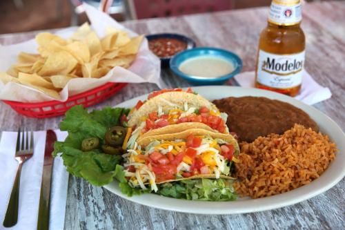 A plate of tacos with lettuce, tomatoes, cheese, rice, refried beans, and jalapeños, accompanied by chips and a beer.