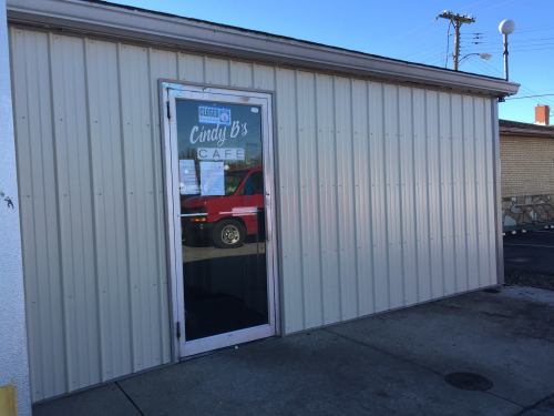 Exterior view of Cindy B's Café, featuring a metal-paneled wall and a glass door with a "CLOSED" sign.
