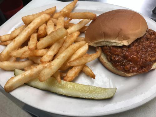 A plate with a sloppy joe sandwich, golden fries, and a pickle slice.