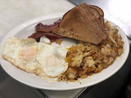A plate of breakfast featuring two fried eggs, crispy hash browns, bacon, and toasted bread.