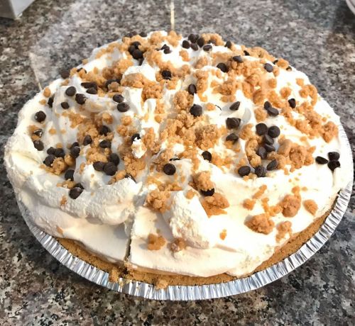 A creamy pie topped with whipped cream, chocolate chips, and crumbled cookies on a silver pie crust.