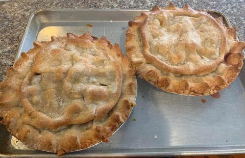 Two freshly baked apple pies on a silver baking tray, dusted with sugar and golden brown crusts.
