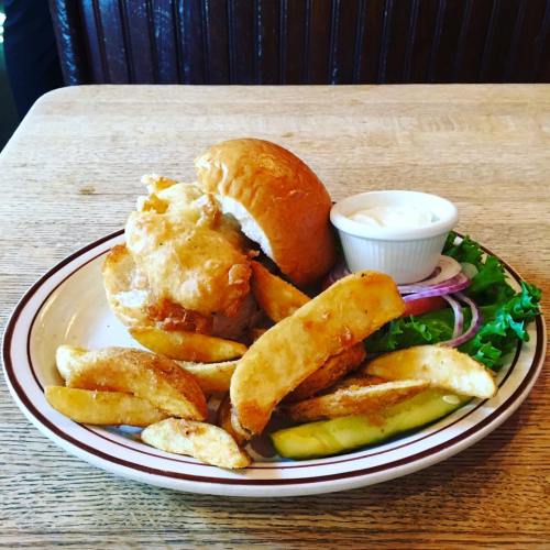 A plate with a sandwich, crispy fried potatoes, lettuce, onion, pickles, and a small bowl of dipping sauce.