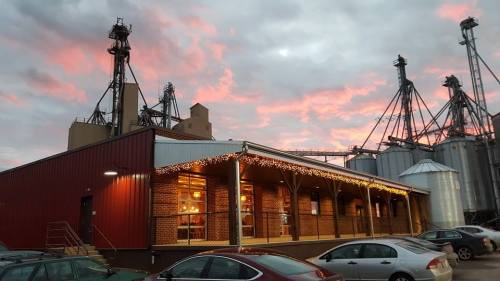 A brick building with festive lights at dusk, surrounded by silos and a colorful sky.