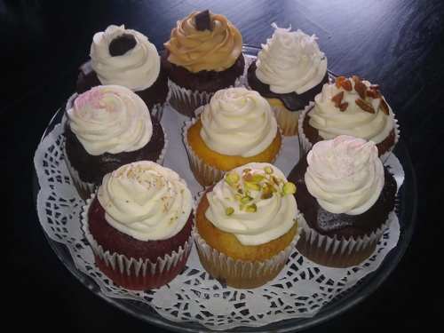 A platter of assorted cupcakes with various frosting designs and toppings, arranged on a lace doily.