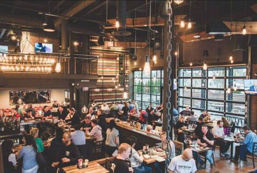 A bustling restaurant interior with diners at tables, large windows, and a warm, inviting atmosphere.