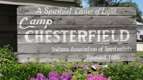 Sign for Camp Chesterfield, a spiritual center in Indiana, established in 1886, surrounded by colorful flowers.