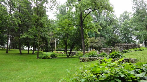 Lush green park with trees, flower beds, and stone features, creating a serene natural landscape.