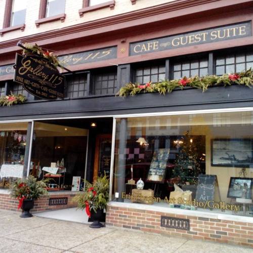 Exterior of Gallery 115, featuring art displays, a café, and holiday decorations on a charming street.