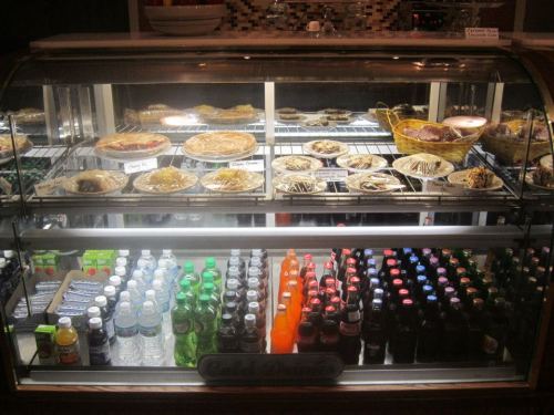 A display case filled with various desserts and drinks, including pies, pastries, and a selection of bottled beverages.