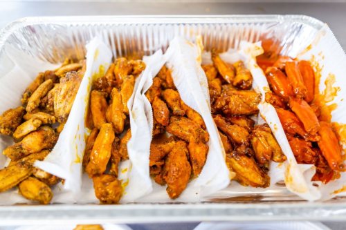 A tray of assorted chicken wings, including different flavors, arranged with paper liners.