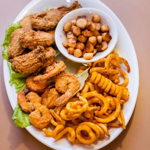 A platter featuring fried chicken, shrimp, curly fries, and a side of diced potatoes.