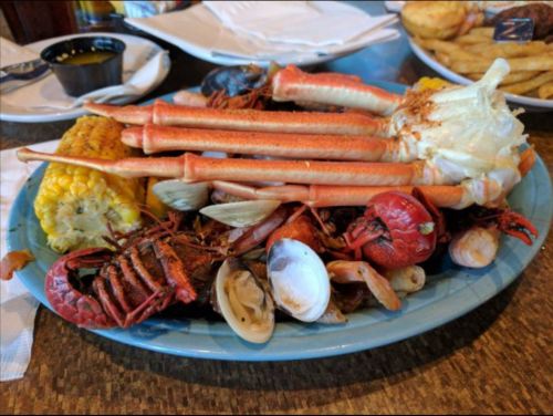 A seafood platter featuring crab legs, crawfish, shrimp, clams, and corn on the cob, served on a blue plate.