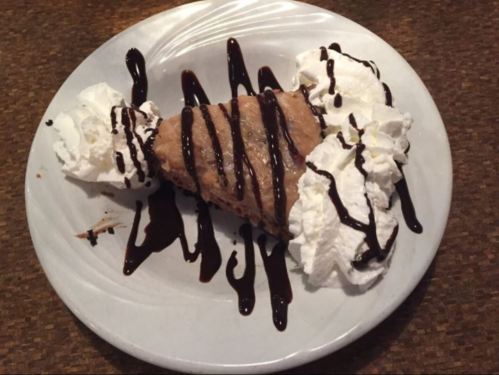 A slice of dessert topped with whipped cream and drizzled with chocolate sauce on a white plate.