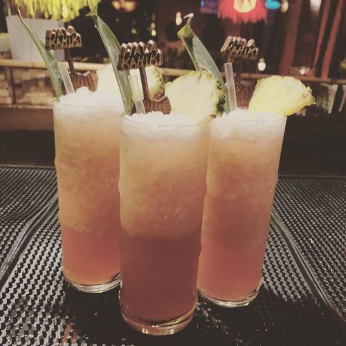 Three colorful cocktails with pineapple garnishes and decorative straws, served in tall glasses on a bar counter.